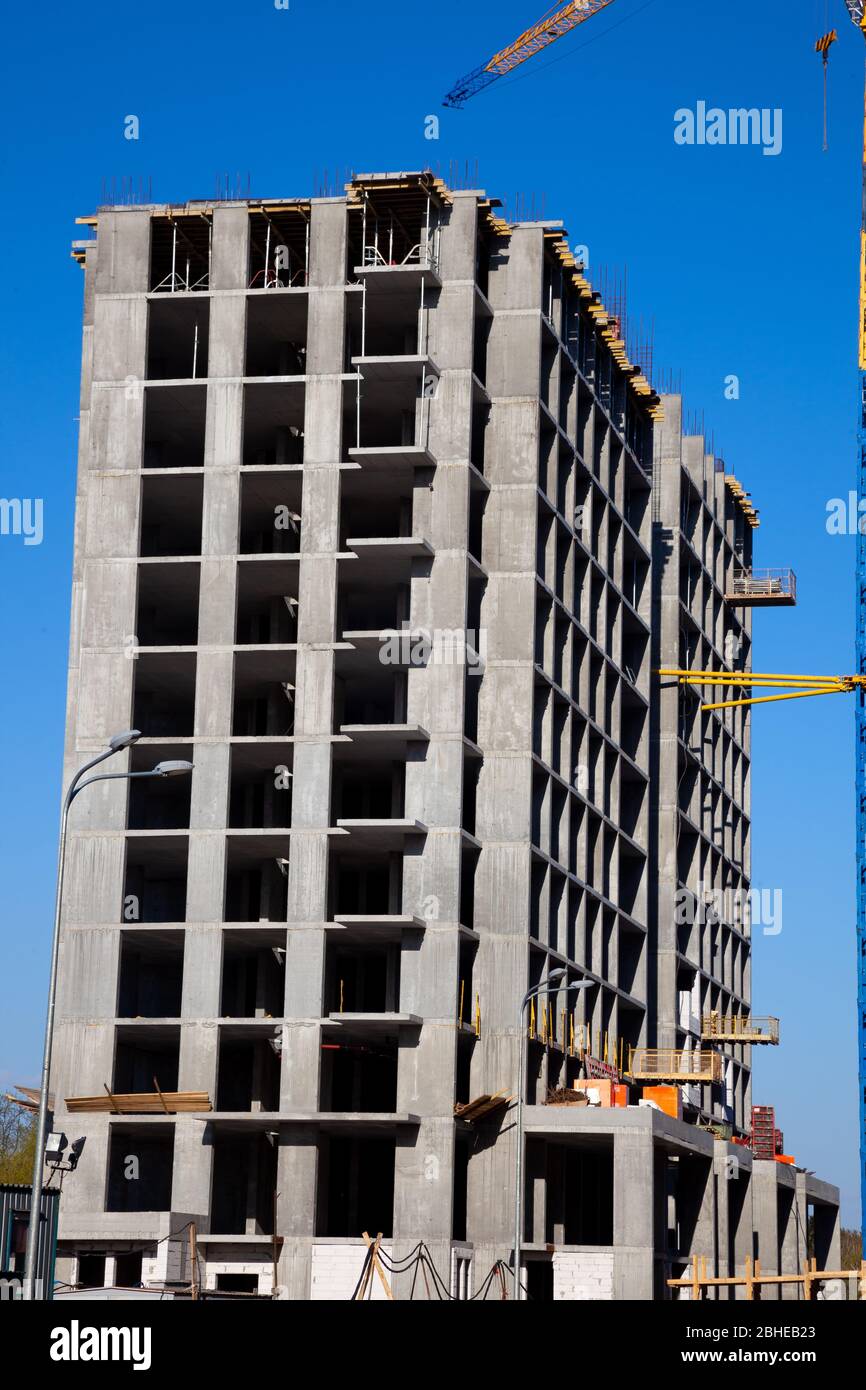 Costruzione di case in cemento. Telaio e gru. La costruzione di un alto edificio residenziale e di un parcheggio. Via. Foto Stock