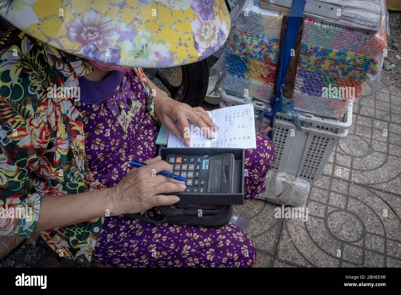 Ho Chi Minh City, Vietnam - 10 aprile 2018: Una donna più vecchia e irriconoscibile che usa una calcolatrice al mercato di un contadino, visto dall'alto Foto Stock