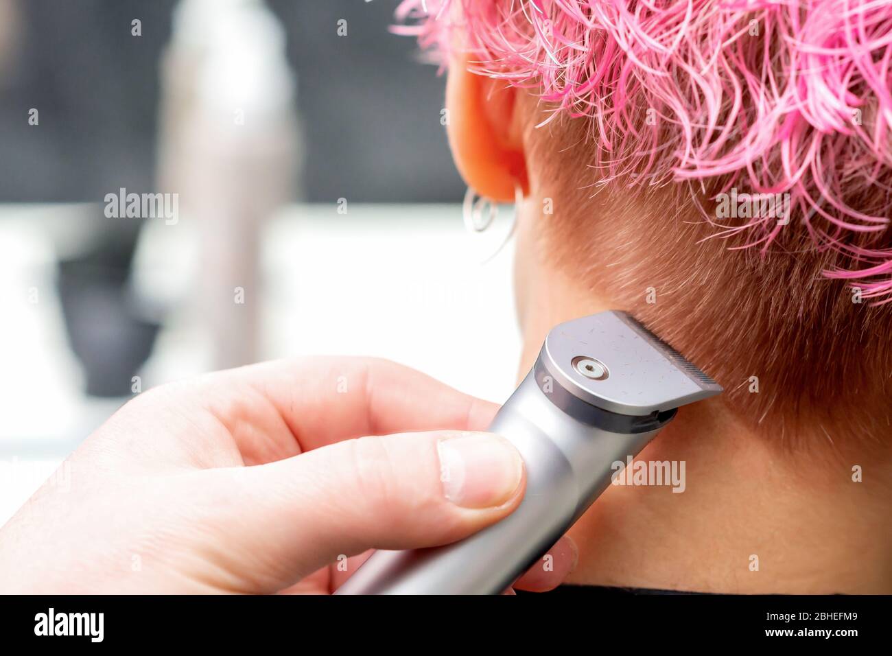 Vista posteriore parrucchiere mano è rasare capelli rosa di donna con  rifinitore elettrico in salone di parrucchiere, primo piano Foto stock -  Alamy