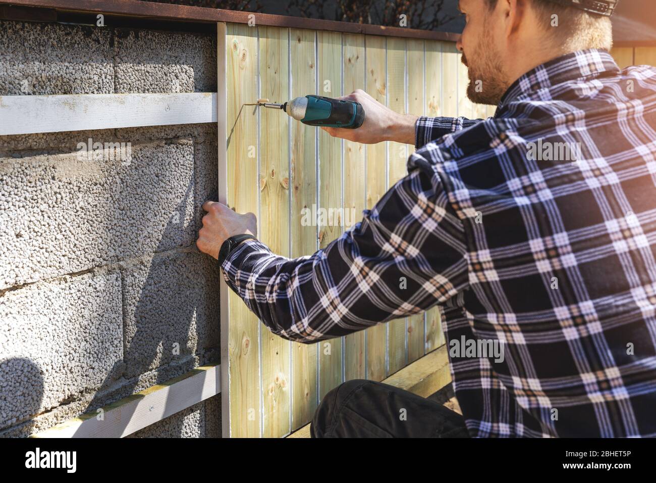 installazione di tavole di legno su muro di blocco di calcestruzzo nel cortile di casa Foto Stock