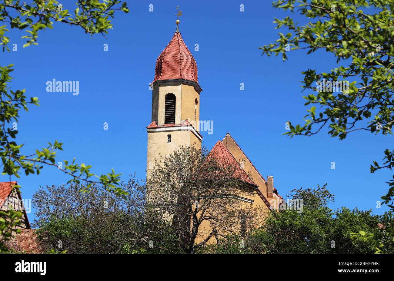 chiesa con torre di cipolla in un villaggio bavarese, incorniciato da alberi, in una giornata di primavera soleggiata Foto Stock