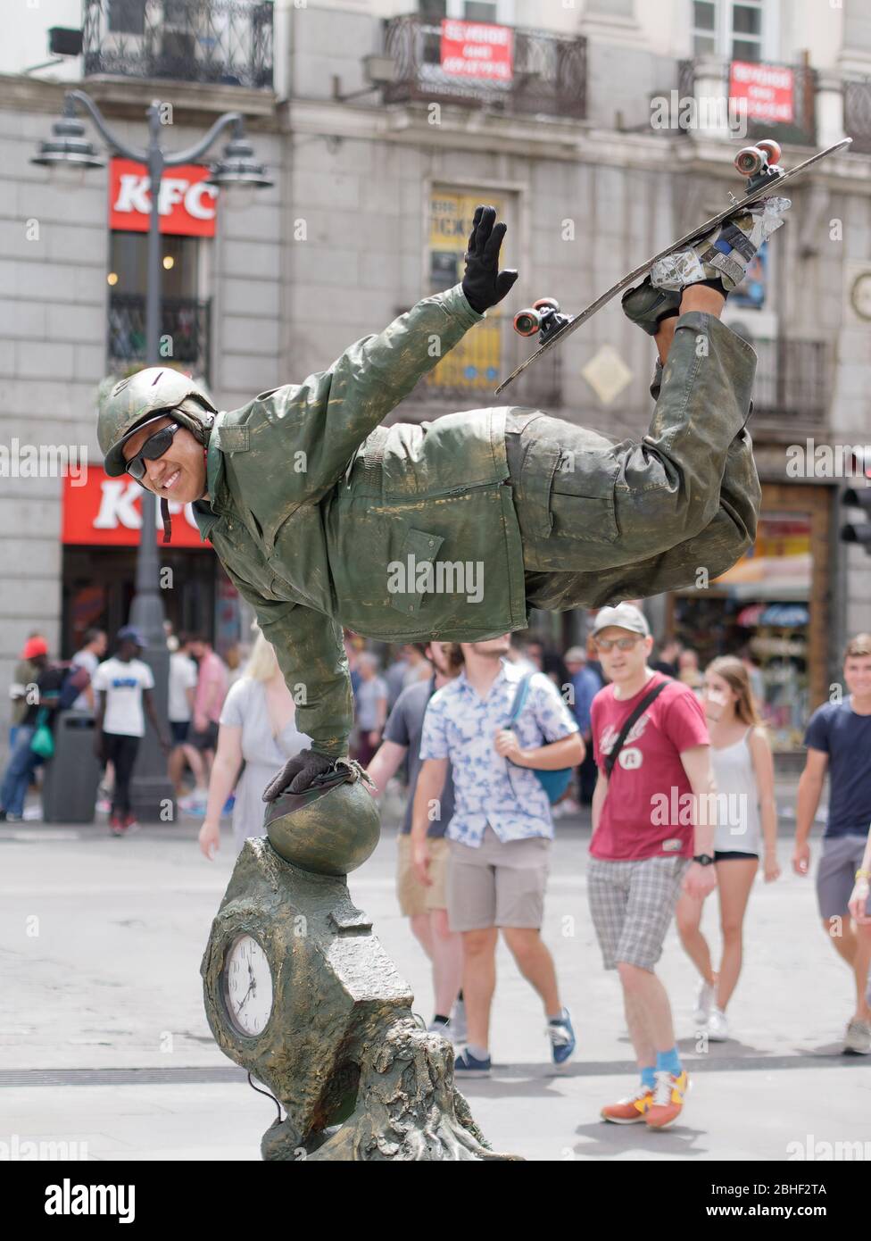 Artista di strada che recita una statua di bronzo di uno skateboarder che mostra il trucco dello skateboard per divertire i turisti a Puerta del Sol. Foto Stock