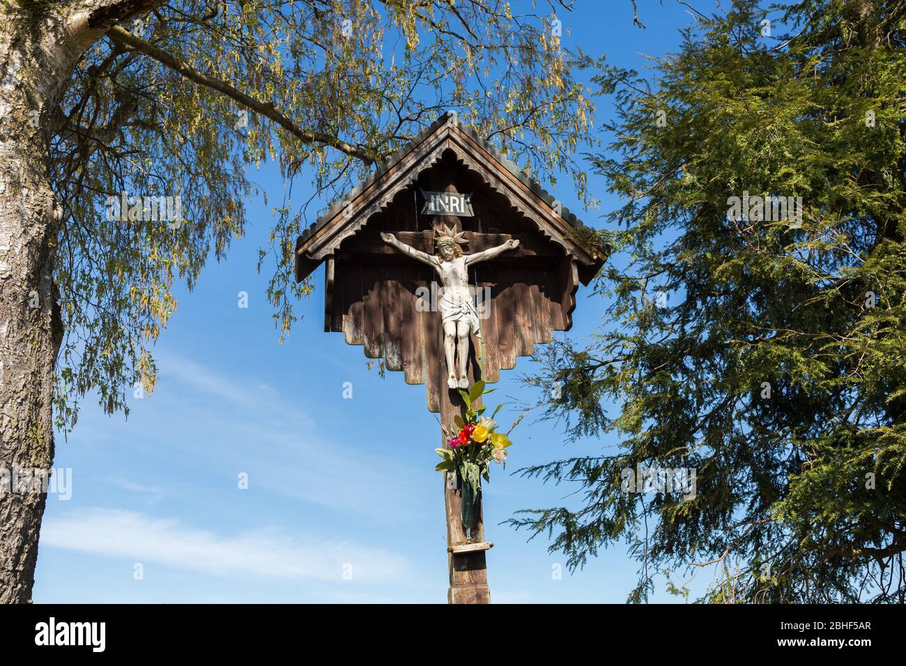 Una vista comune quando si fa un'escursione attraverso la Baviera: Gesù sulla croce. Scultura bianca, scolpita in legno. Con tetto piccolo come protezione. Foto Stock