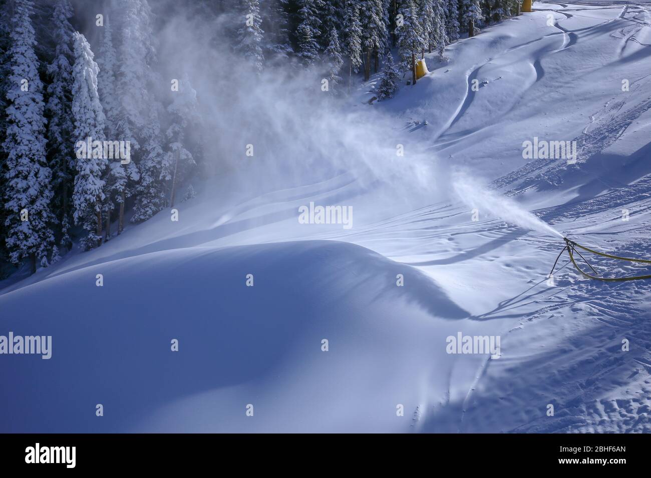 Attrezzatura per la produzione della neve che soffia la neve su una pista da sci e forma una grande banca della neve Foto Stock