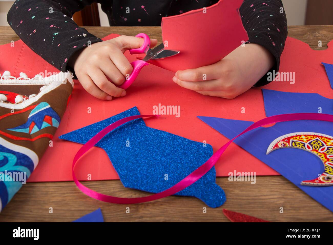 Primo piano delle mani dei bambini preparare la decorazione domestica di Ramadan usando carta colorata - diy Ramadan zeena e lanterna fatte a mano Foto Stock
