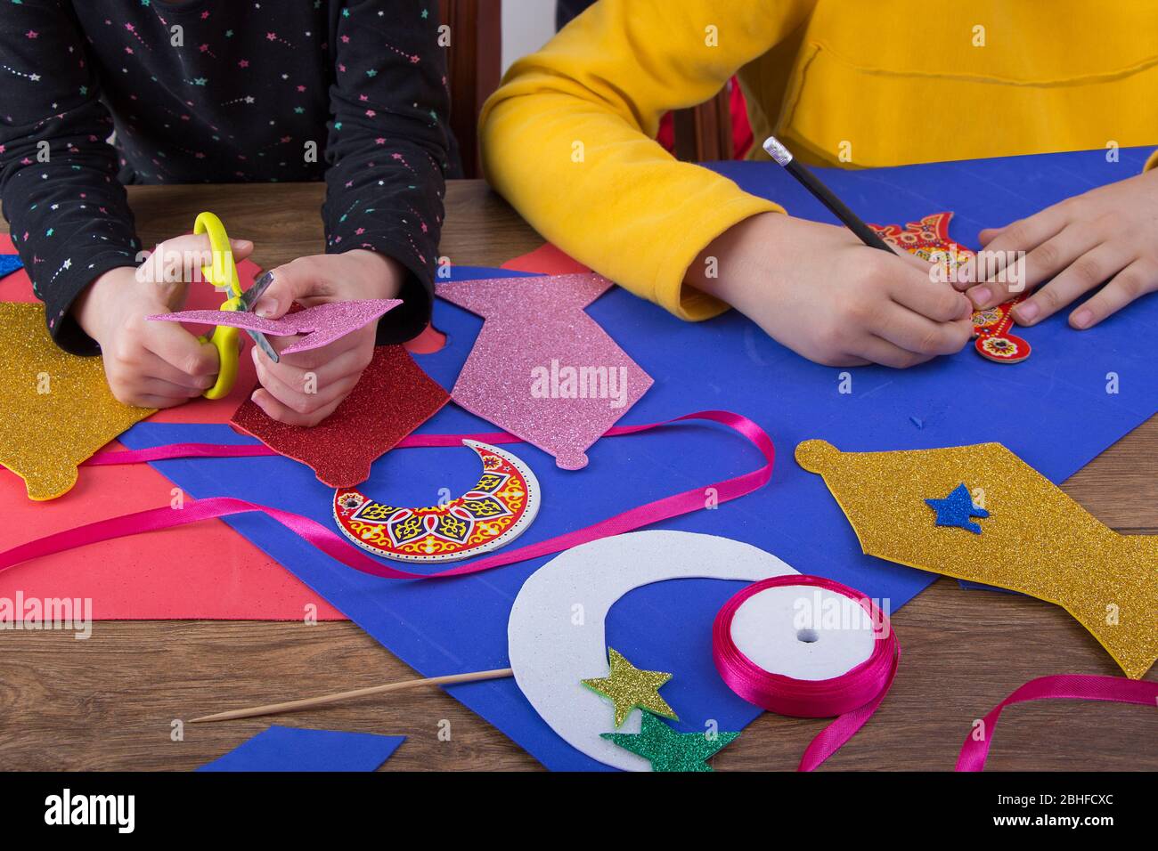 Primo piano delle mani dei bambini preparare la decorazione domestica di Ramadan usando carta colorata - diy Ramadan zeena e lanterna fatte a mano Foto Stock