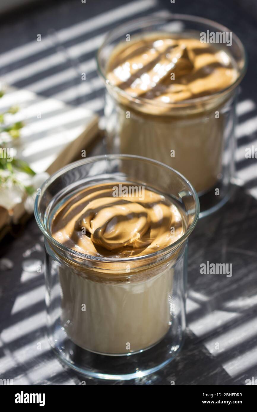 Dalgona caffè in bicchieri trasparenti su davanzale illuminato dalla luce del sole. Foto Stock