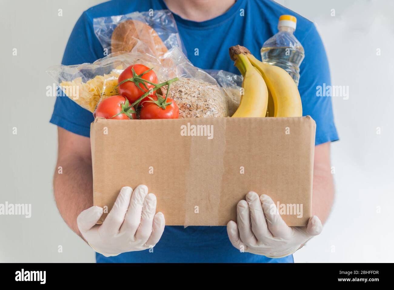 Uomo in camicia blu e guanti di gomma tiene la scatola con il cibo. Consegna di cibo di donazione Foto Stock