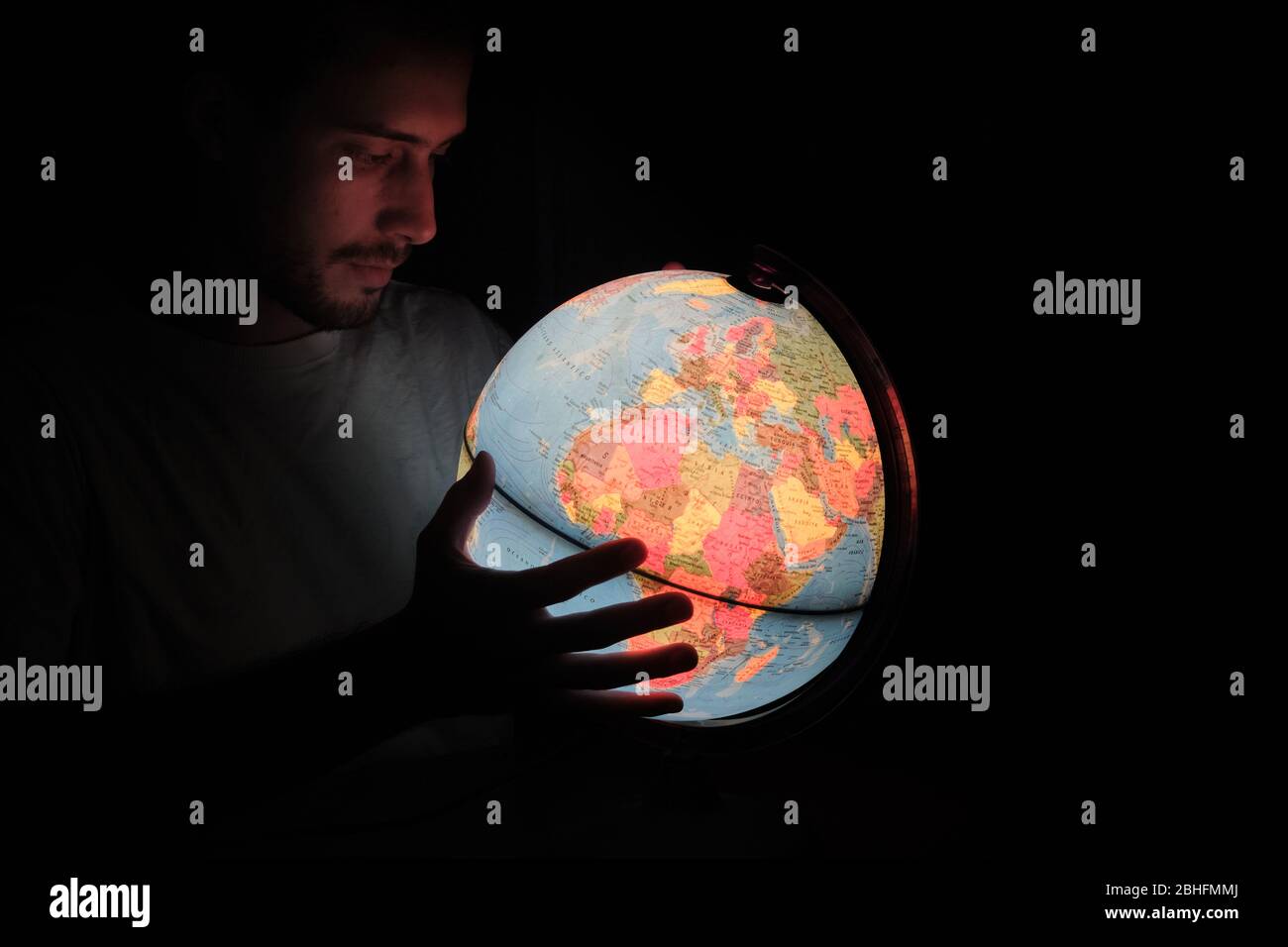Un uomo che guarda un globo rotante Terra lampada luce illuminata scrivania Mappa Geografia nella notte buia con il volto illuminato Foto Stock