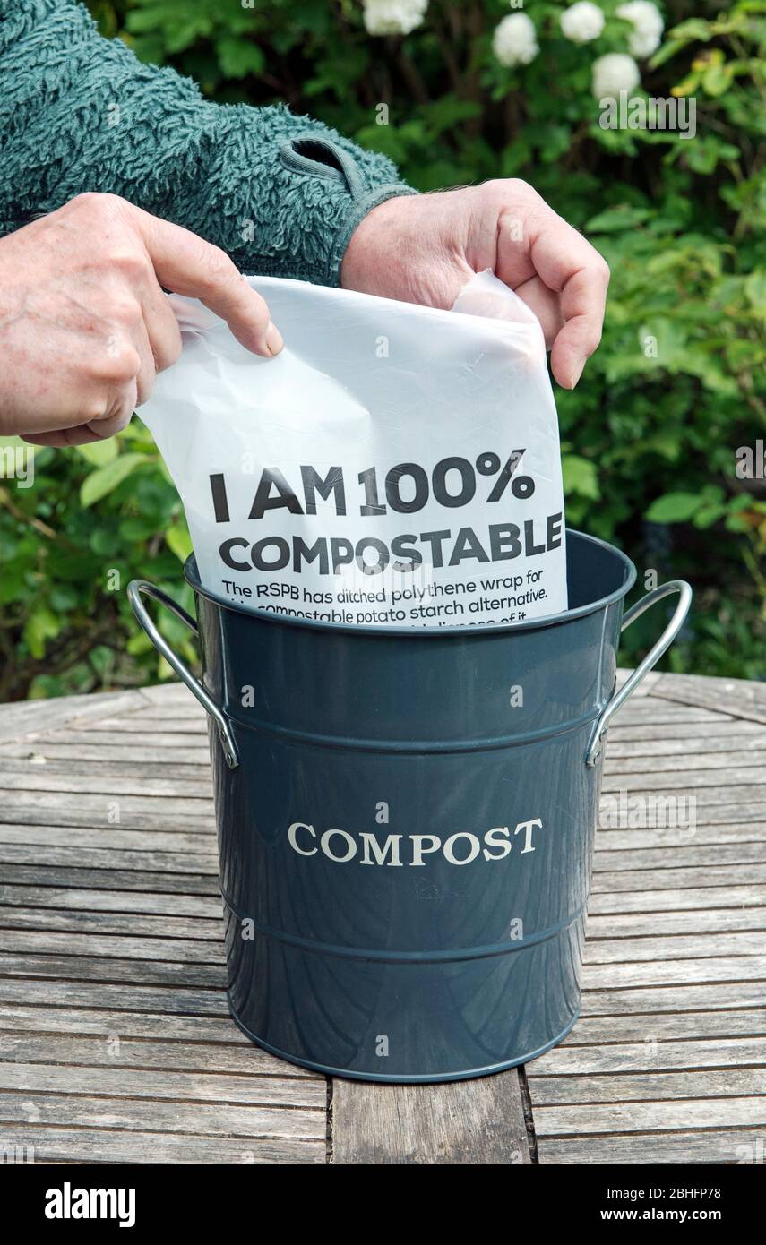 Cestino di composto di rivestimento dell'uomo con imballaggio o imballaggio della rivista compostabile fatto di amido di patate che dice 'sono 100% compostable' sul tavolo da giardino. Zero sprechi Foto Stock