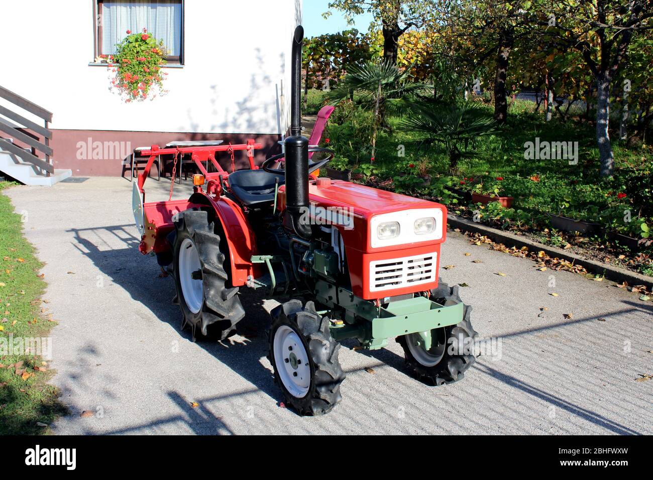 Rinnovato e riverniciato vintage retrò vecchio piccolo trattore compatto con nuovi pneumatici parcheggiati su strada asfaltata di casa di famiglia suburbana Foto Stock