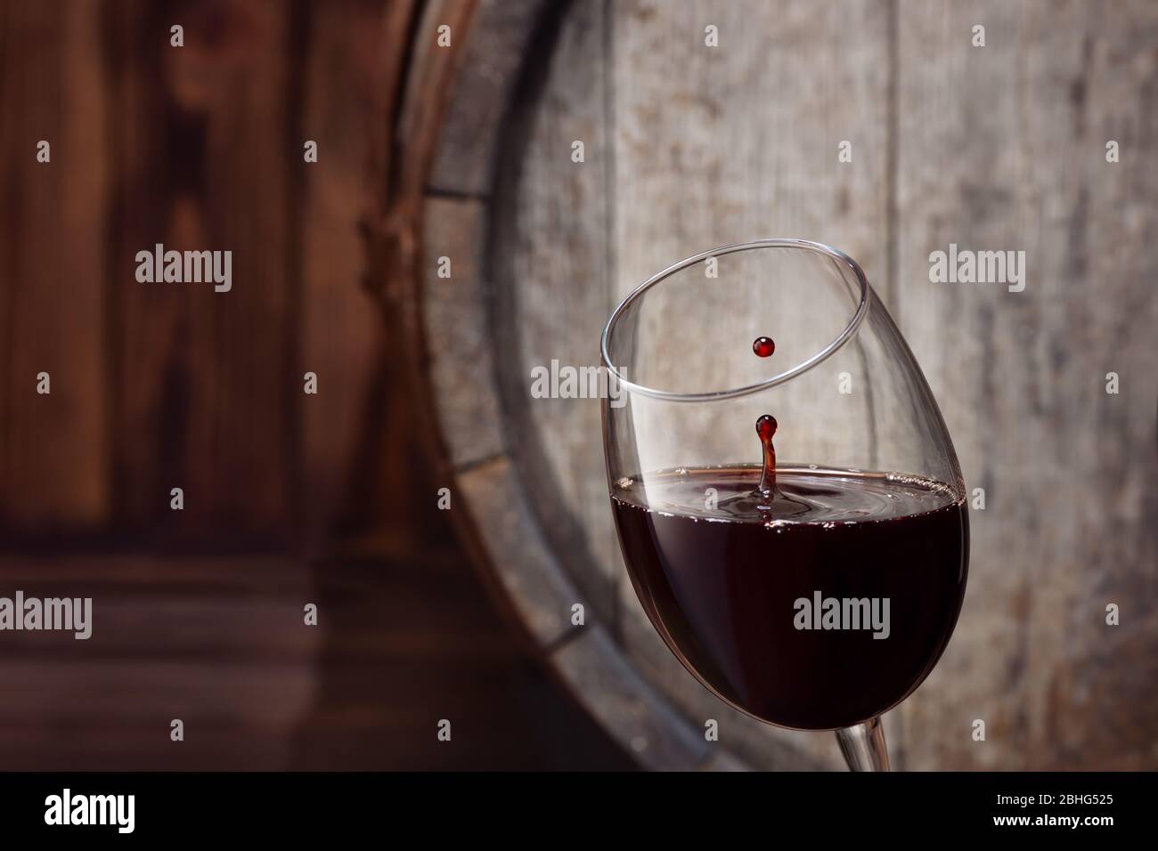 spruzzare vino rosso in vetro con vecchio barile di legno come sfondo Foto Stock