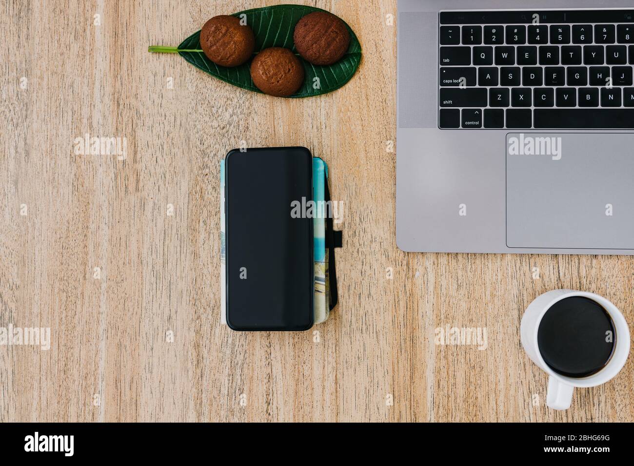 Disposizione piatta del luogo di lavoro. Smartphone e appunti per il lavoro freelance. Caffè del mattino con biscotti. Spazio di copia su sfondo di legno e blocco note. A Foto Stock