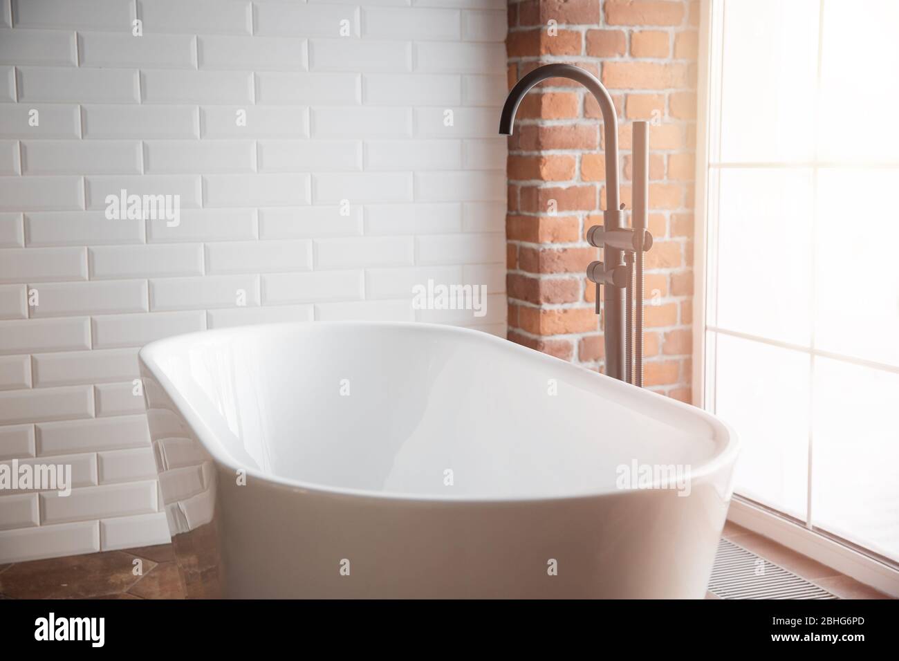 Bagno moderno con vasca bianca indipendente e rubinetto nero. Pareti in mattoni in stile loft Foto Stock