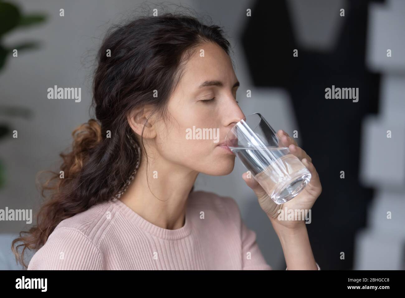 Tranquilla donna millenaria bere vetro di acqua distillata pura. Foto Stock