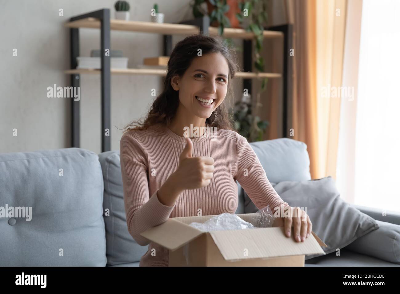 Donna felice che tiene la scatola in grembo, mostrando i pollici in su gesto. Foto Stock