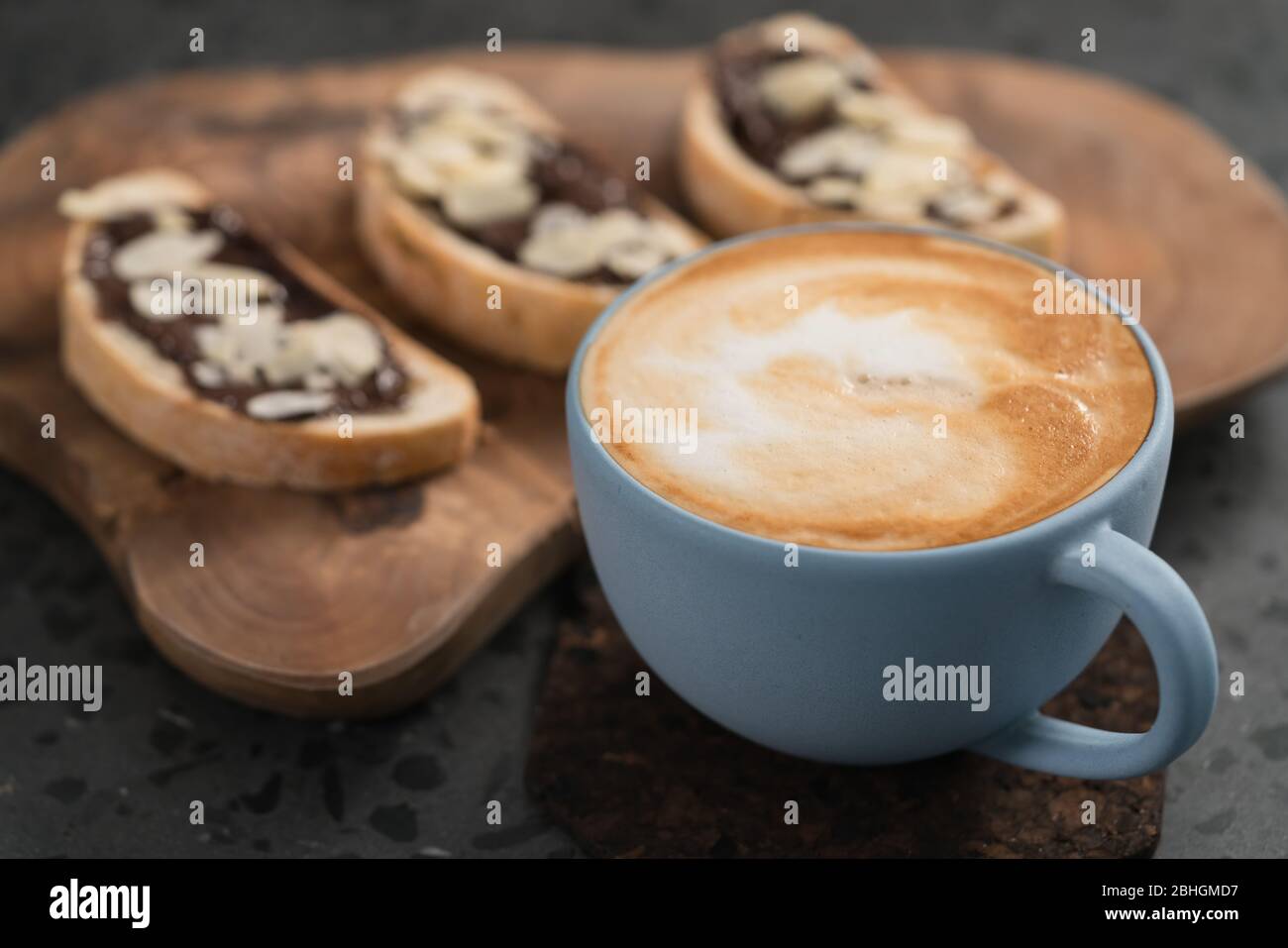Cappuccino fresco in tazza blu con tostature con crema di cioccolato su sfondo concreto Foto Stock