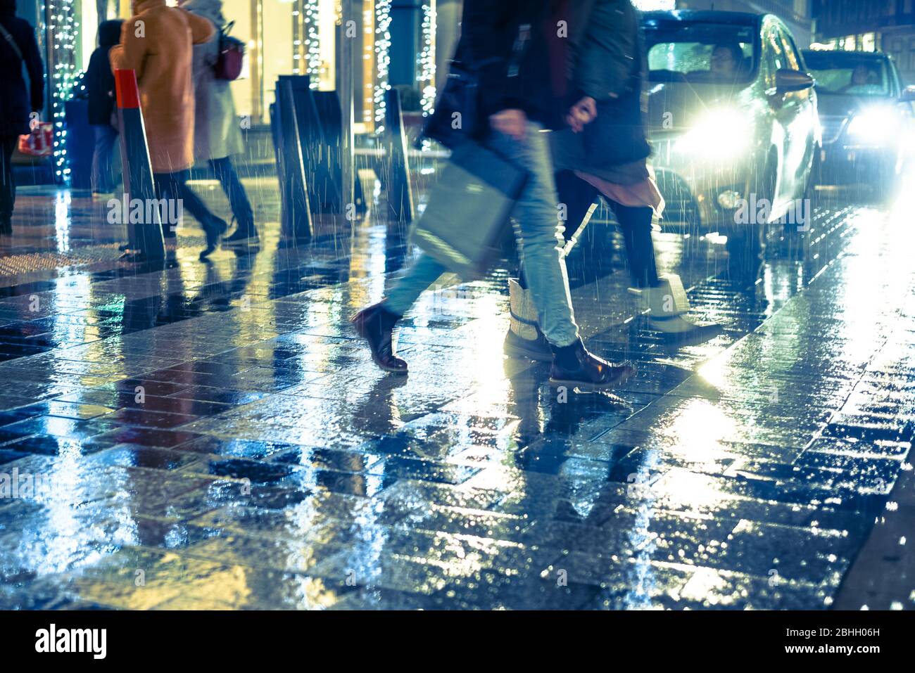 La gente che trasporta le borse di shopping attraversa la strada della città sotto la pioggia di notte Foto Stock