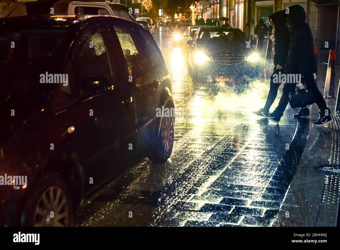 Coppia nelle cappe attraversare la strada di notte sotto la pioggia Foto Stock