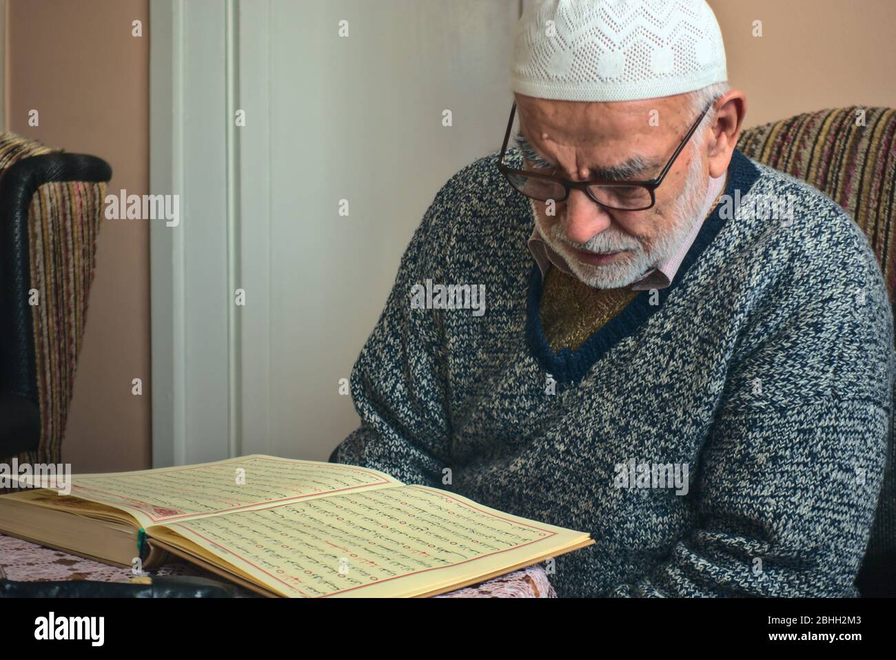 Ankara/Turkey - 24.04.2020: Un uomo musulmano turco molto vecchio che indossa una cuffia di preghiera recitando il libro più sacro, Qur'an nel mese di Ramadan Foto Stock
