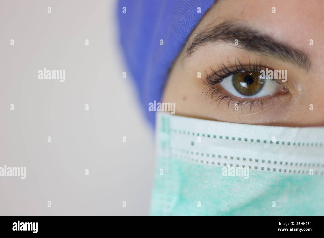 vista frontale della mezza faccia dell'infermiere in ospedale, protetta con maschera e cappuccio per coronavirus. Foto Stock