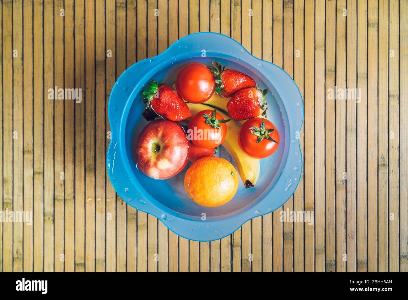 Ciotola blu con frutta fresca e pulita su una base di legno. Banane, pomodori, mele, fragole e arance immerse nell'acqua. Foto Stock