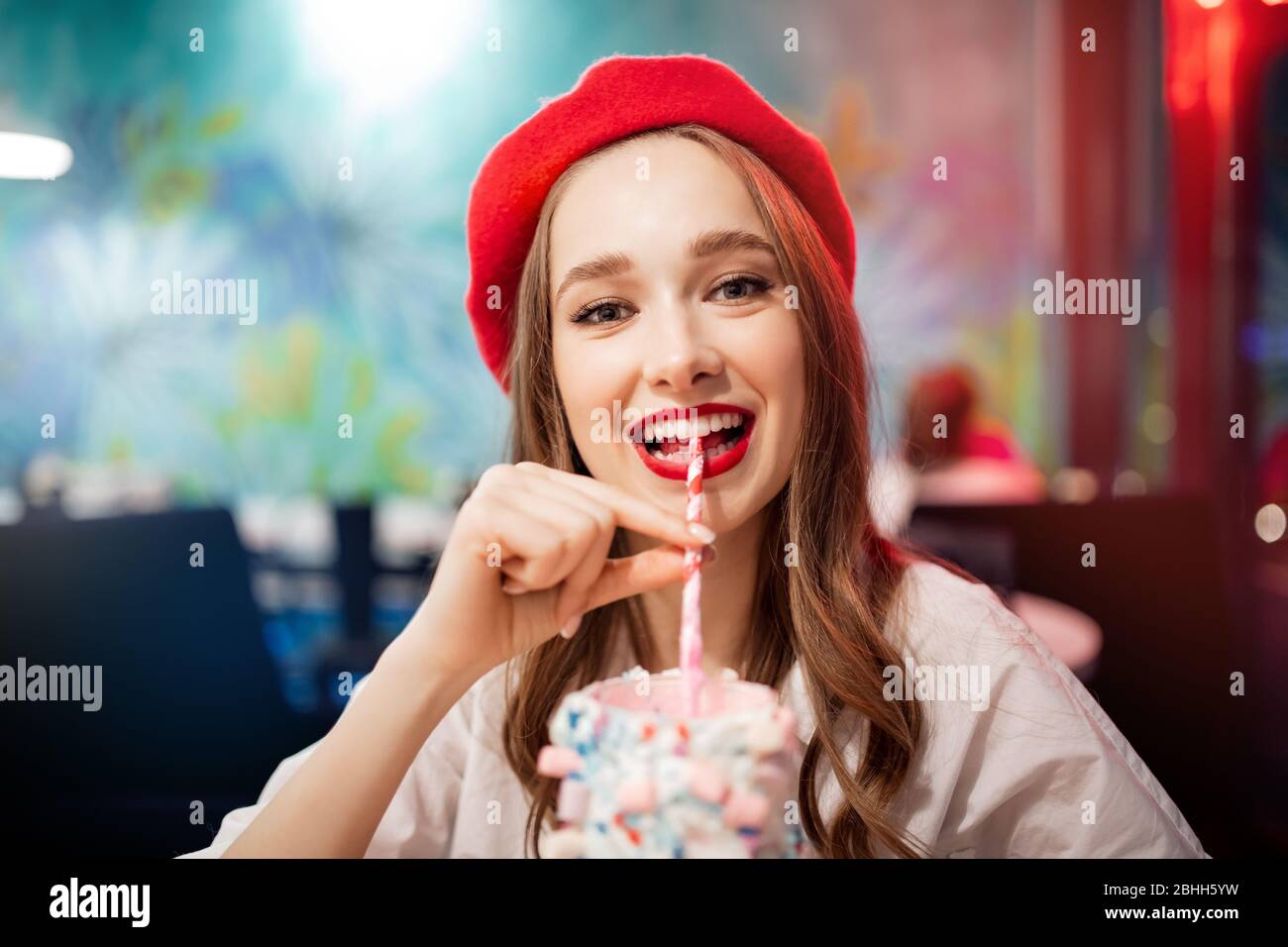Ragazza con denti bianchi, bel sorriso in berretto rosso, Francia bevande rosa fragola milkshake dalla paglia Foto Stock
