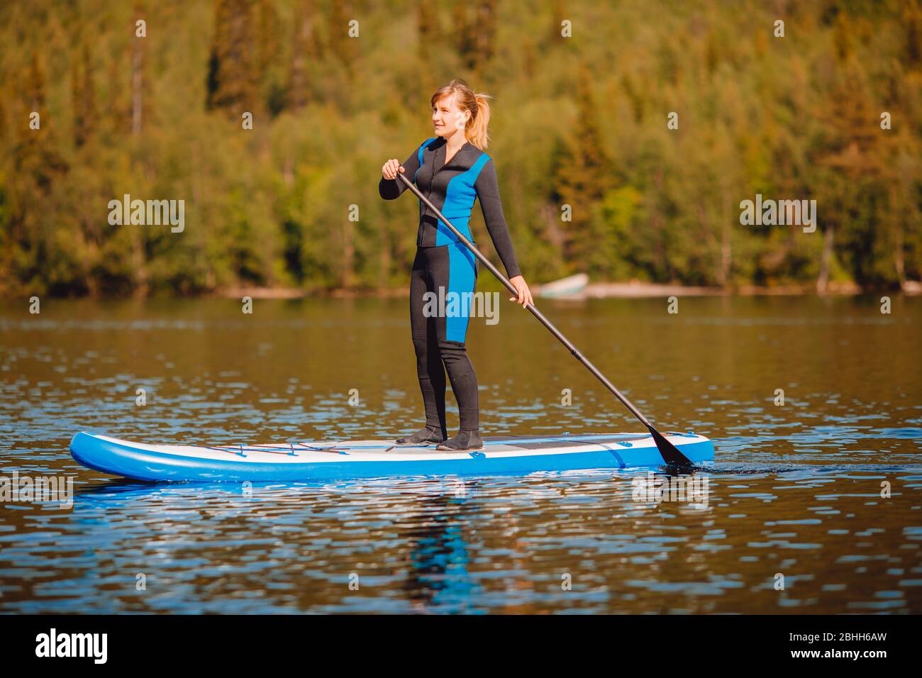 La ragazza di termo abbigliamento remo canottaggio sul sup pensione lago  blu acqua paddleboard sfondo della foresta Foto stock - Alamy