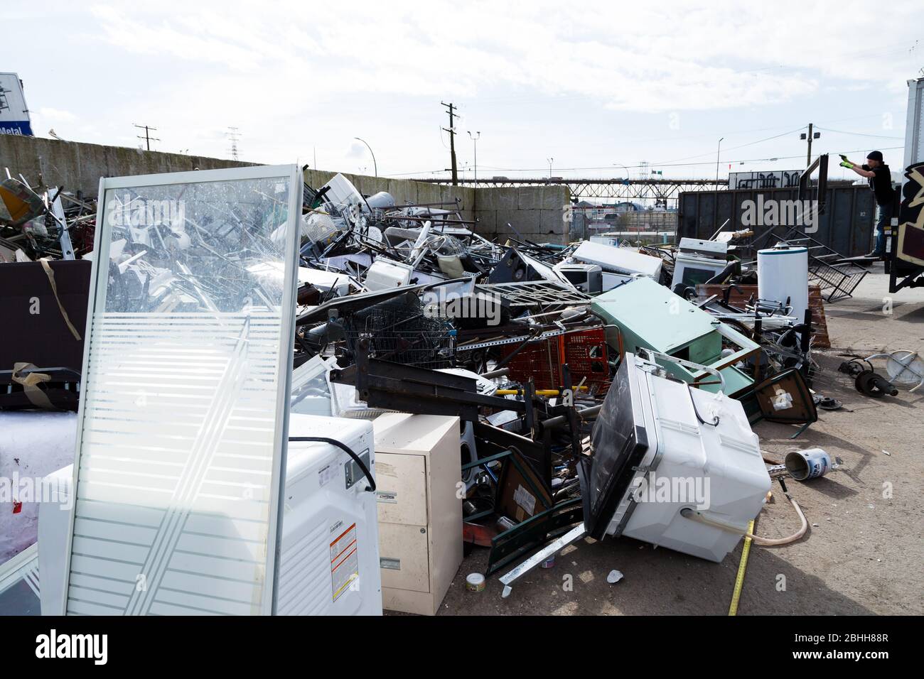 Un lavoratore che lancia rifiuti in un cumulo di rottami metallici in un centro di riciclaggio. Foto Stock