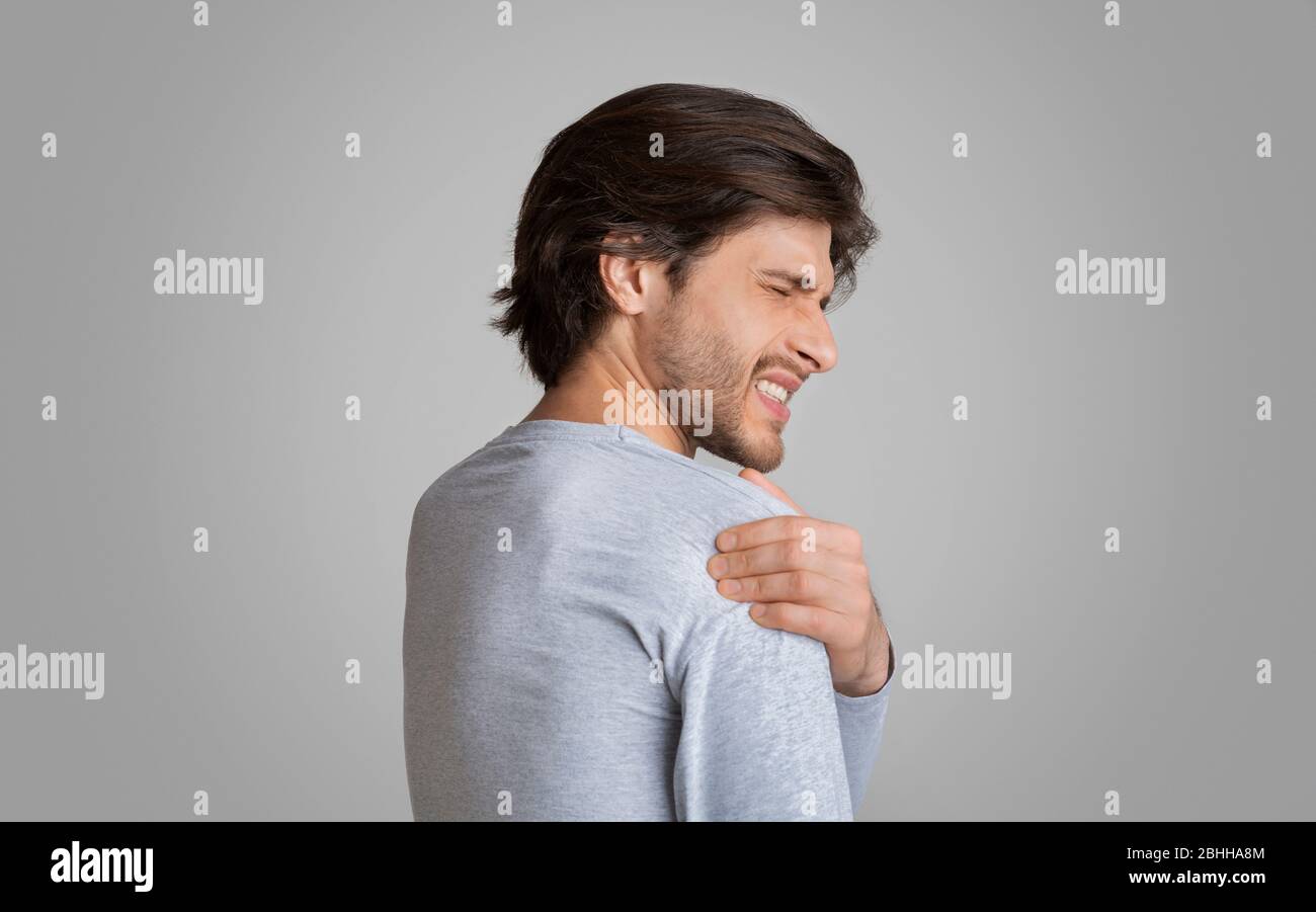 L'uomo con espressione dolorosa, sfrega la spalla con la mano Foto Stock