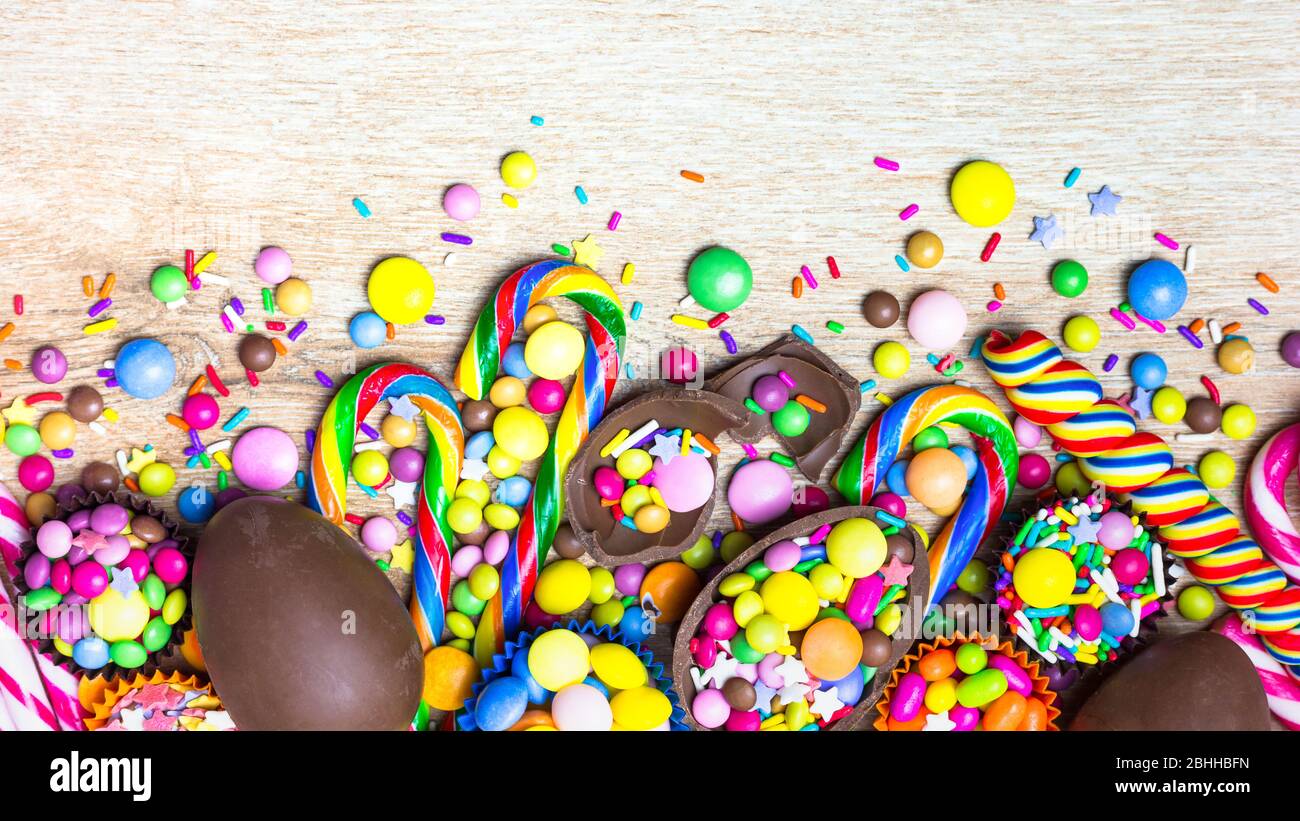 Caramelle colorate, uova di cioccolato e lecca lollipopps su sfondo di legno. Vista dall'alto con spazio per le copie. Foto Stock