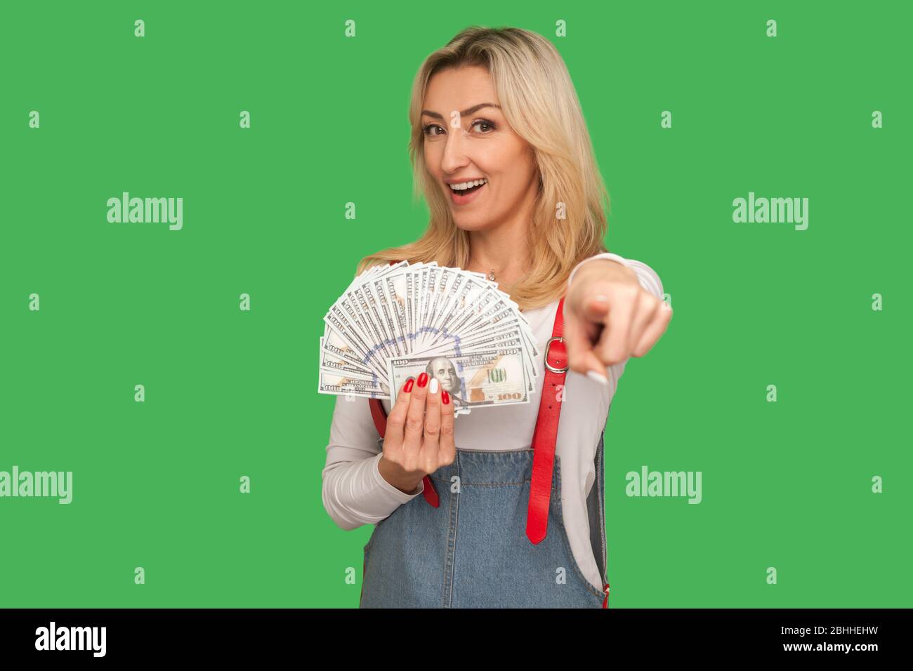 Ehi, vuoi grandi soldi? Ritratto di donna adulto positivo in tute di stile tenendo banconote dollaro e puntando a macchina fotografica, banca pubblicitaria loa Foto Stock