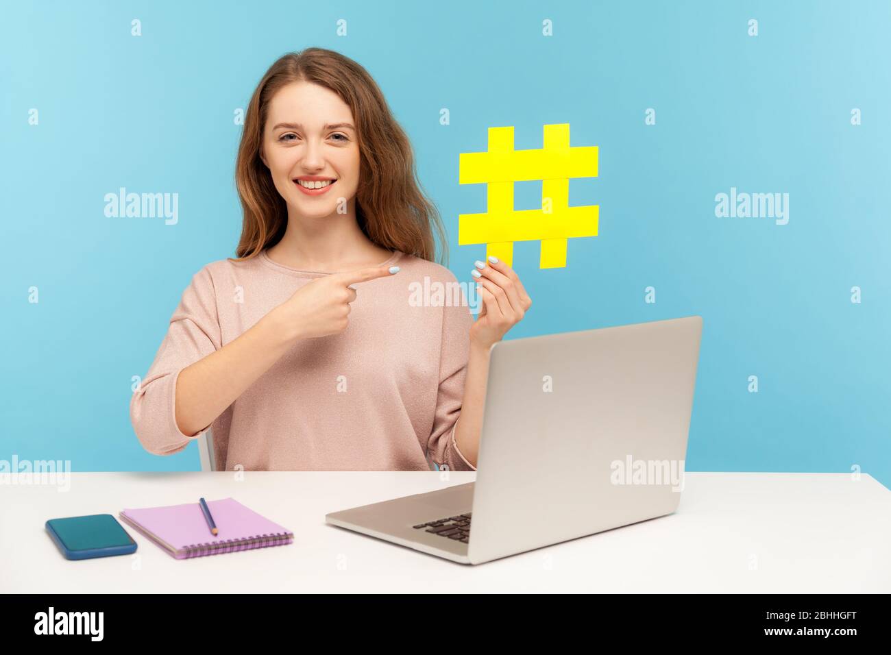 Promozione di pagine Web, tendenze virali. Felice donna sorridente che indica il simbolo giallo grande hashtag, seo smm marketing manager che lavora su notebook in ufficio a casa. Foto Stock