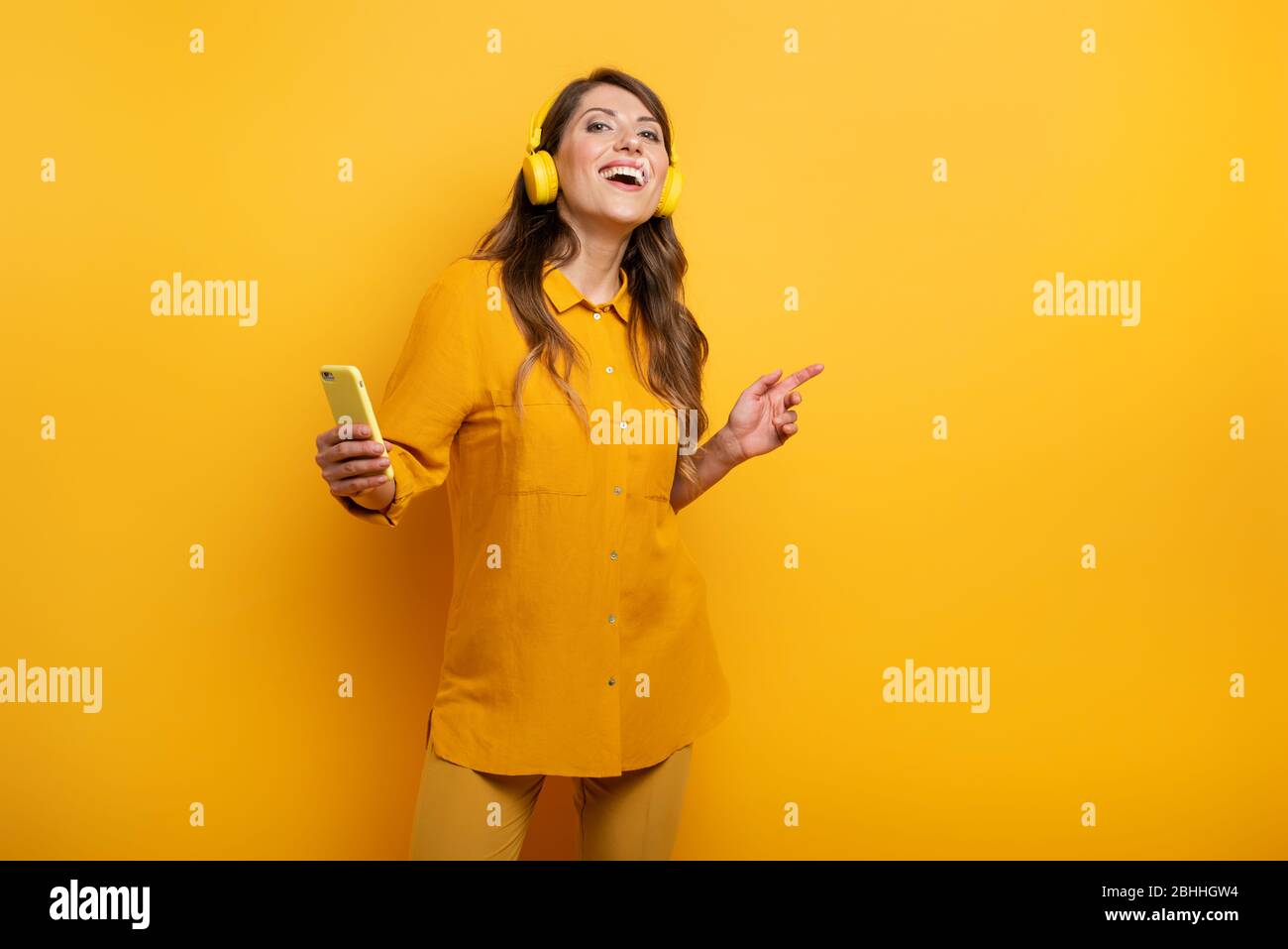 Ragazza con auricolare giallo ascolta musica e danze. emozionale e espressione energica Foto Stock