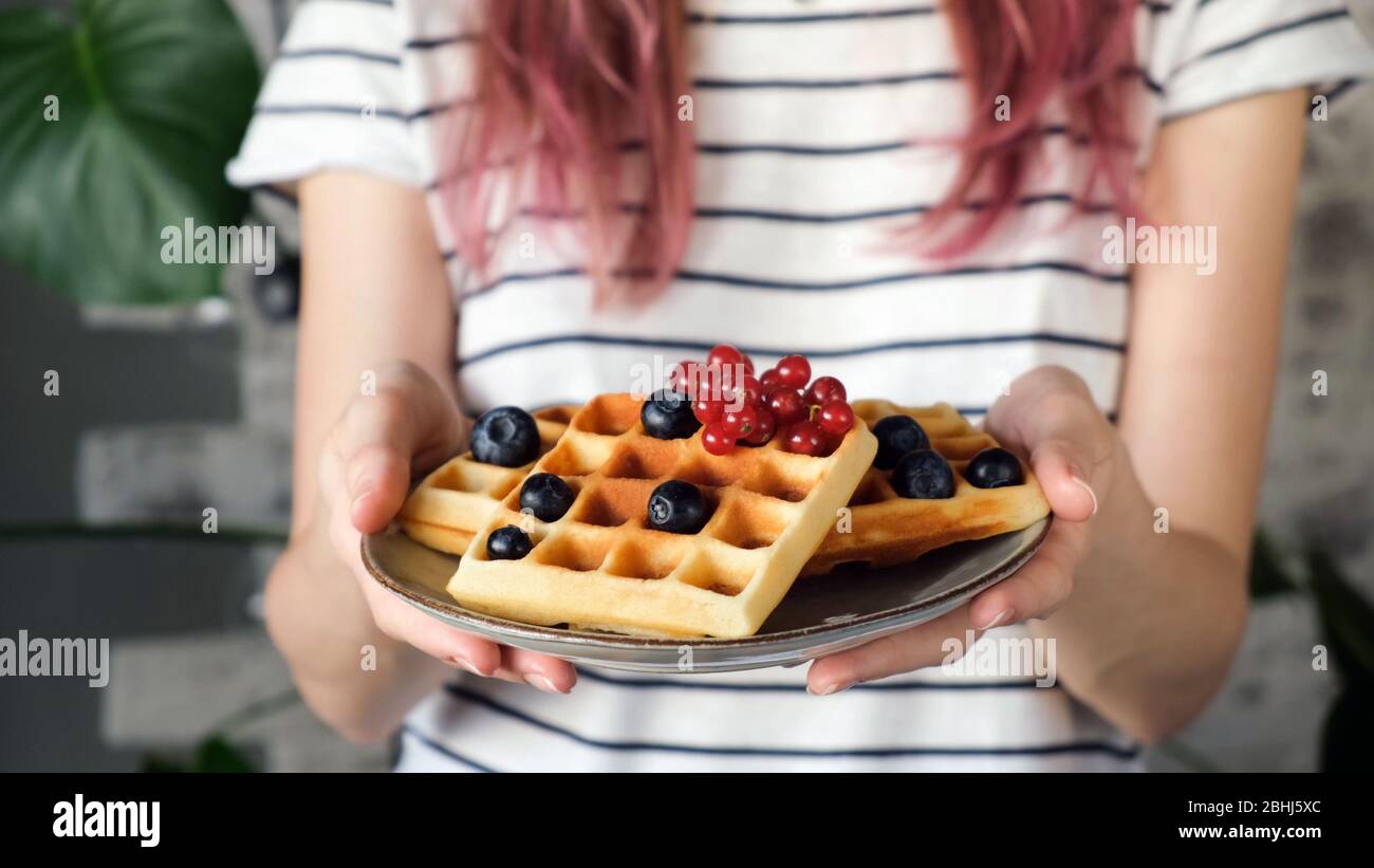 Piatto di waffle belgi in mano femminile. Hipster girl con capelli rosa che tiene waffle Foto Stock
