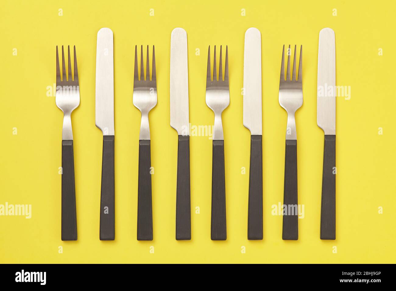 Coltello e forchetta neri su sfondo giallo. Vista dall'alto Foto Stock