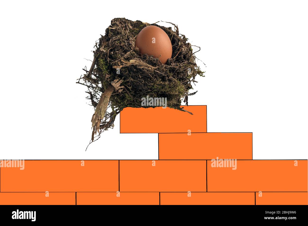 Nido d'uccello contenente un uovo di pollo che si siede precariosamente su un muro di mattoni rossi. Concetto: Costruire un uovo nido, investimento solido, valore patrimoniale, rischio. Foto Stock
