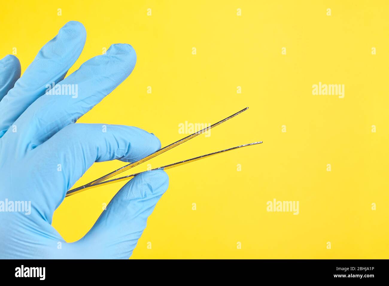 Mano di medico in guanto medico blu che tiene una pinzetta isolata su sfondo giallo Foto Stock