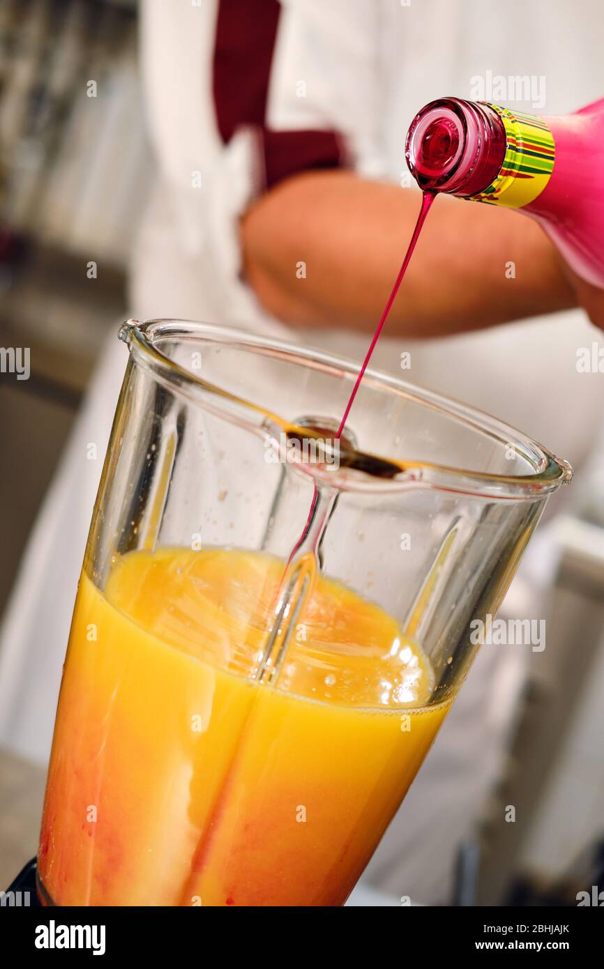 Il barman fa il cocktail, il flacone di acqua con sciroppo di granatina che si versa in succo d'arancia miscela ingredienti immagine ravvicinata, persona irriconoscibile Foto Stock
