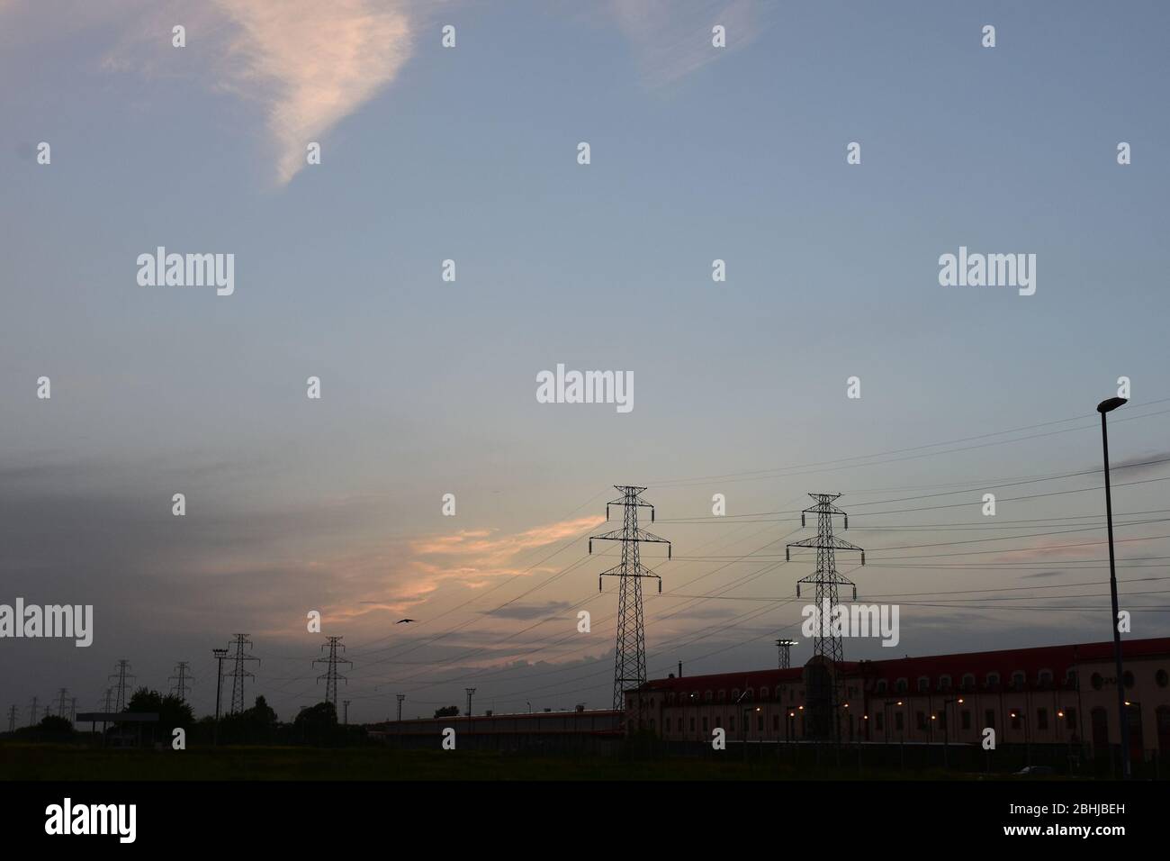 Crepuscolo su un'area piana con basso edificio e linee ad alta potenza in serie Foto Stock