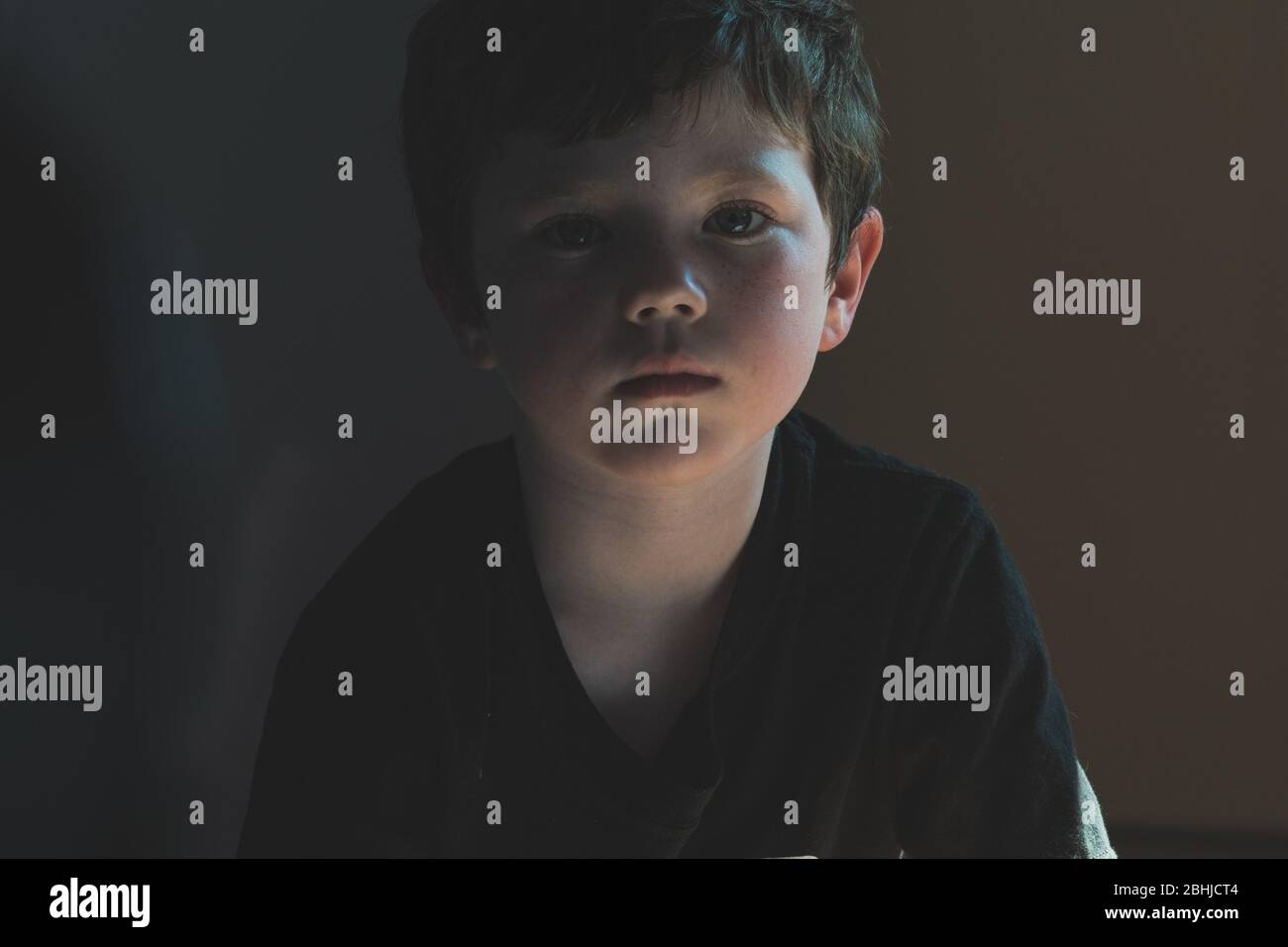 Giovane ragazzo caucasico in una t-shirt nera guardando direttamente la macchina fotografica che appare triste e sconvolto Foto Stock