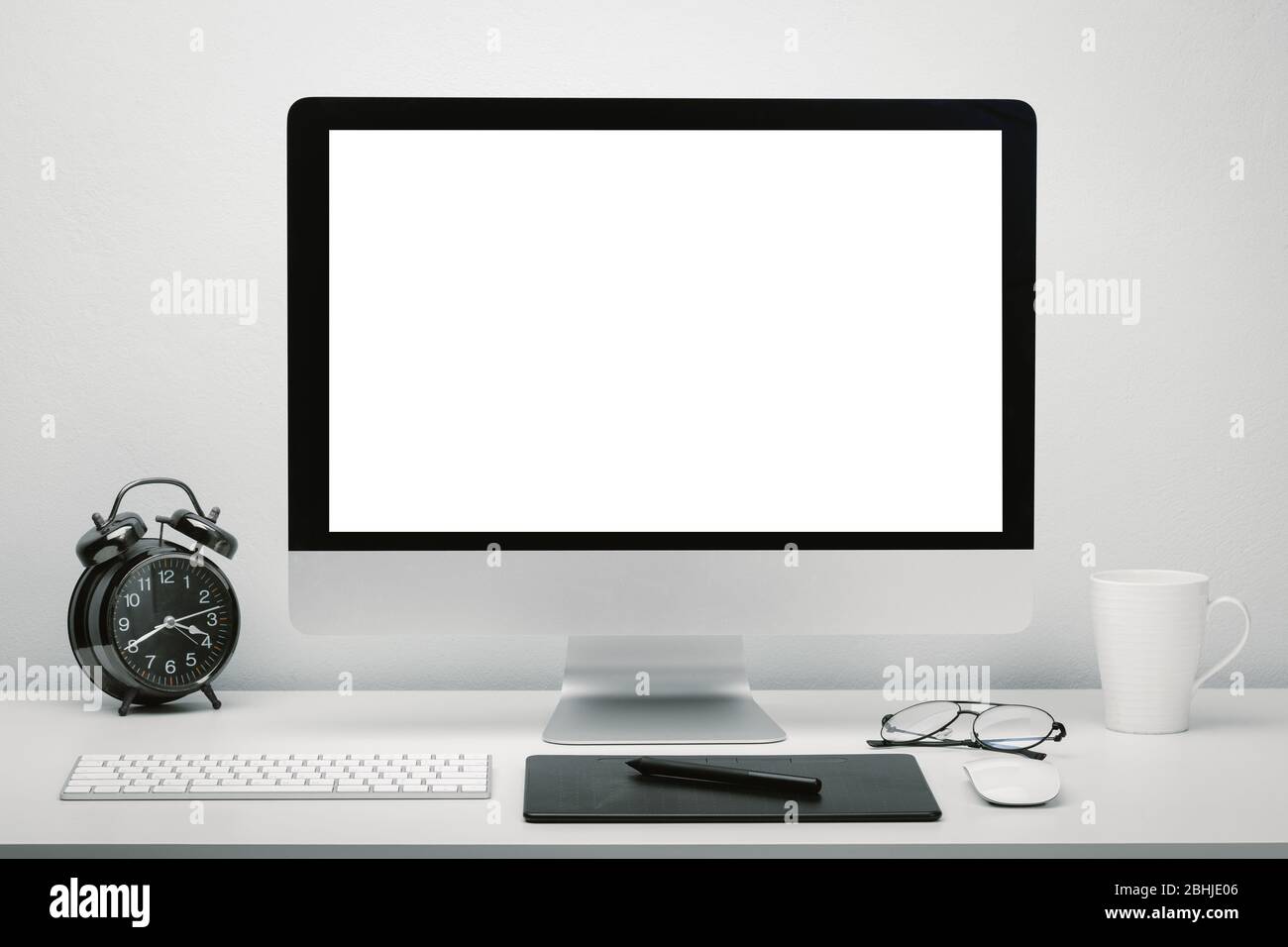 Elegante area di lavoro con schermo vuoto per computer da scrivania con tastiera, mouse, tazza di caffè, orologio, occhiali e penna tablet. Foto Stock