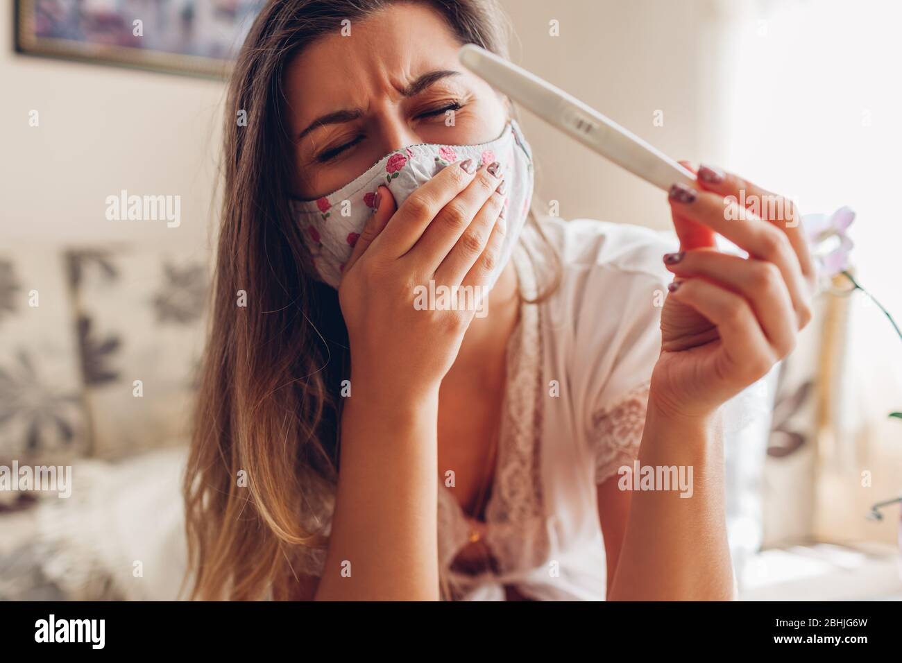 Gravidanza durante la pandemia di coronavirus covid-19. Donna malata in maschera controllo positivo test di gravidanza a casa tosse. Foto Stock