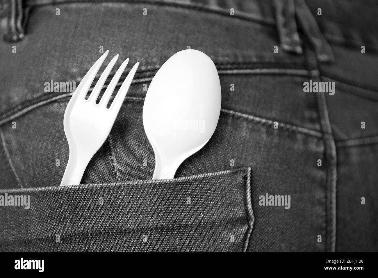 Scopri il concetto di cibo con i jeans denim blu con forchetta bianca e cucchiaio in tasca. Cucchiaio e forchetta in plastica riutilizzabili in tasca. Ambiente sicuro Foto Stock