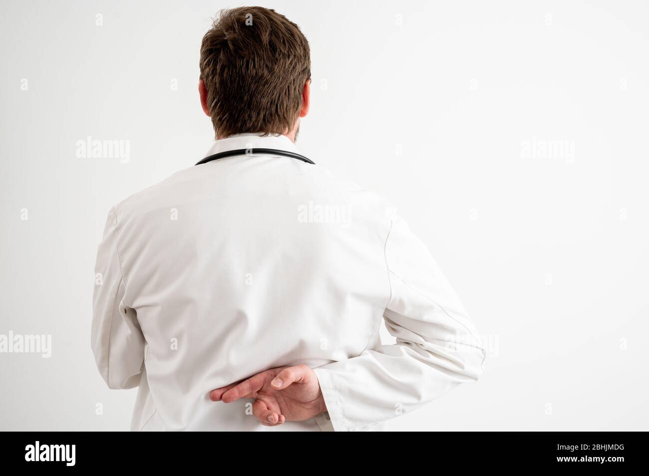 Ritratto di medico maschile con stetoscopio in uniforme medica che mostra il dito trasversale da dietro posando su un fondo bianco isolato Foto Stock