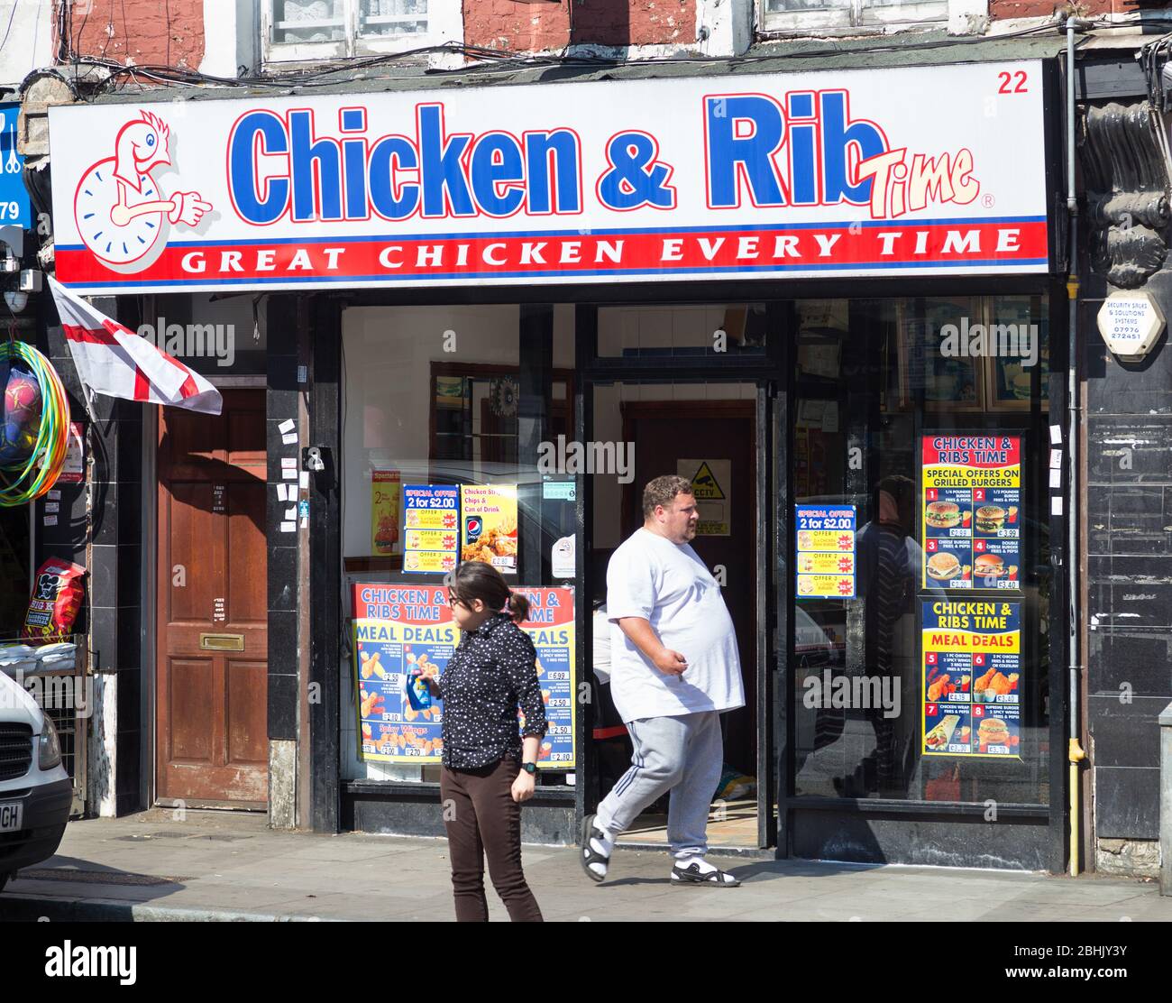 Fat man cammina accanto al negozio di pollo a Kentish Town, a nord di Londra, Regno Unito Foto Stock
