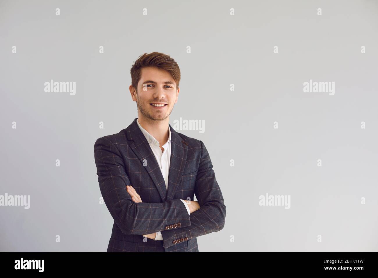 Un uomo sorridente ha attraversato le braccia in una giacca casual su uno sfondo grigio. Foto Stock