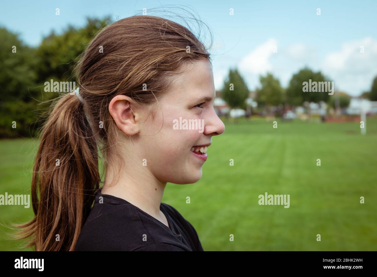 Una ragazza adolescente sportiva con coda di ponytail in profilo in un parco pubblico e campo di calcio Foto Stock