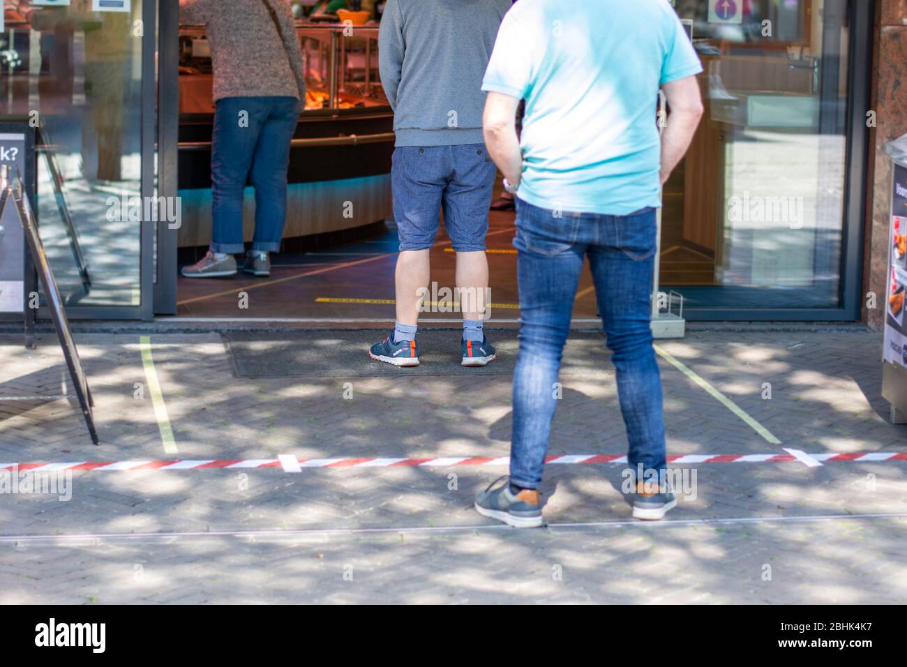 Nastro messo sul pavimento per assicurare che le persone siano distanziate l'una dall'altra. Distanza sociale delle persone che attendono in coda davanti a un negozio di alimentari Foto Stock