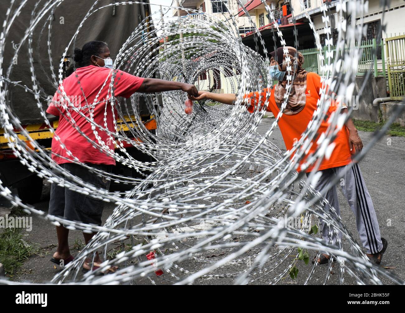 Selayang, Selangor, Malesia. 26 aprile 2020. Una donna raccoglie le forniture attraverso una recinzione di filo spinato a Selayang Baru. Il governo malese ha ora imposto la settima fase dell’Enhanced Movement Control Order (EMCO). Credit: Kepy/ZUMA Wire/Alamy Live News Foto Stock